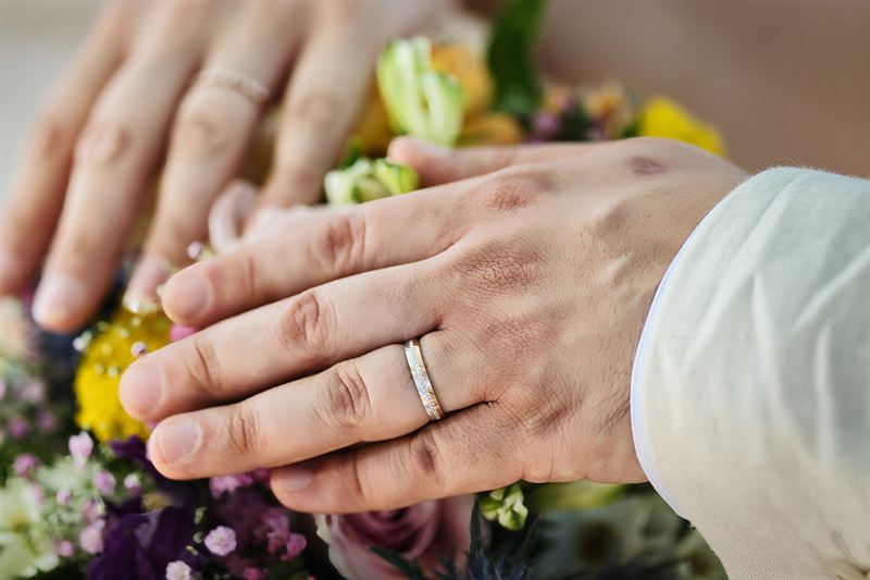 Mains des mariés et alliances posées sur le bouquet